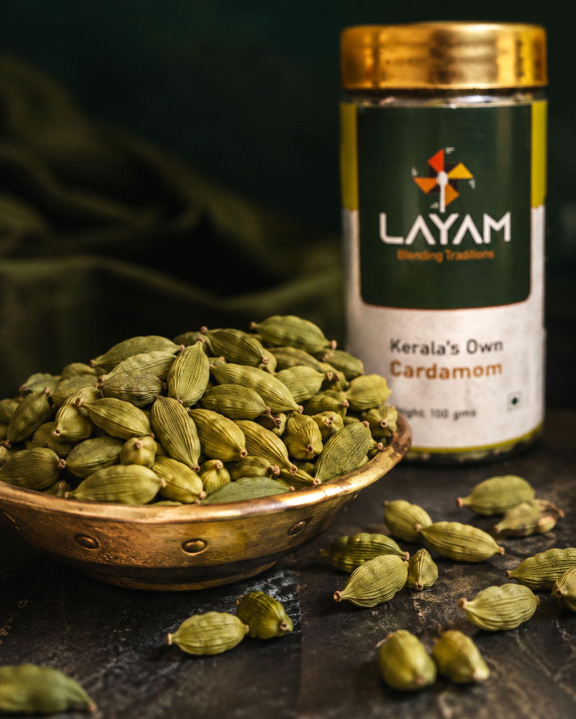Close-up of plump whole green cardamom pods in a copper bowl beside the LAYAM cardamom jar