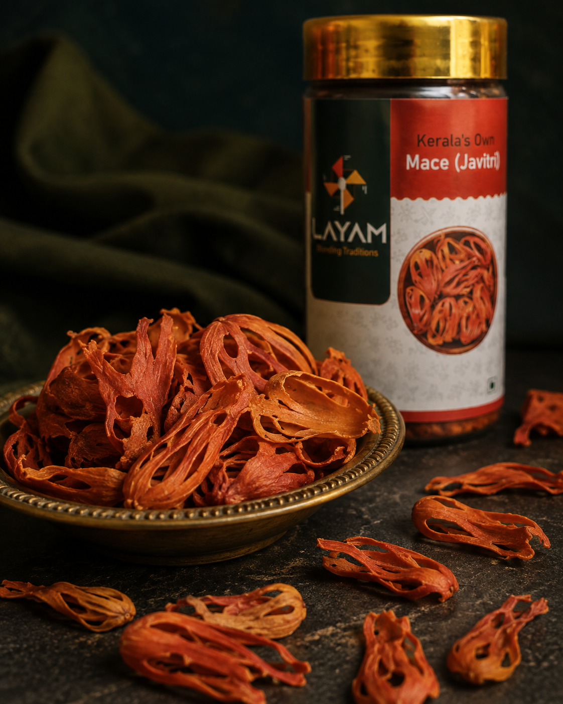 Close-up of whole lacy red mace blades in a brass dish beside the LAYAM mace jar