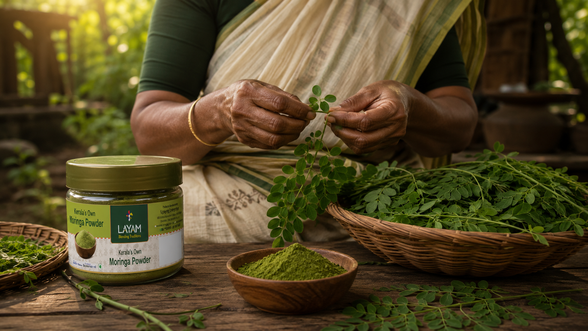 A woman hand-picking fresh moringa leaves in Kerala, with a basket of leaves and the LAYAM jar alongside