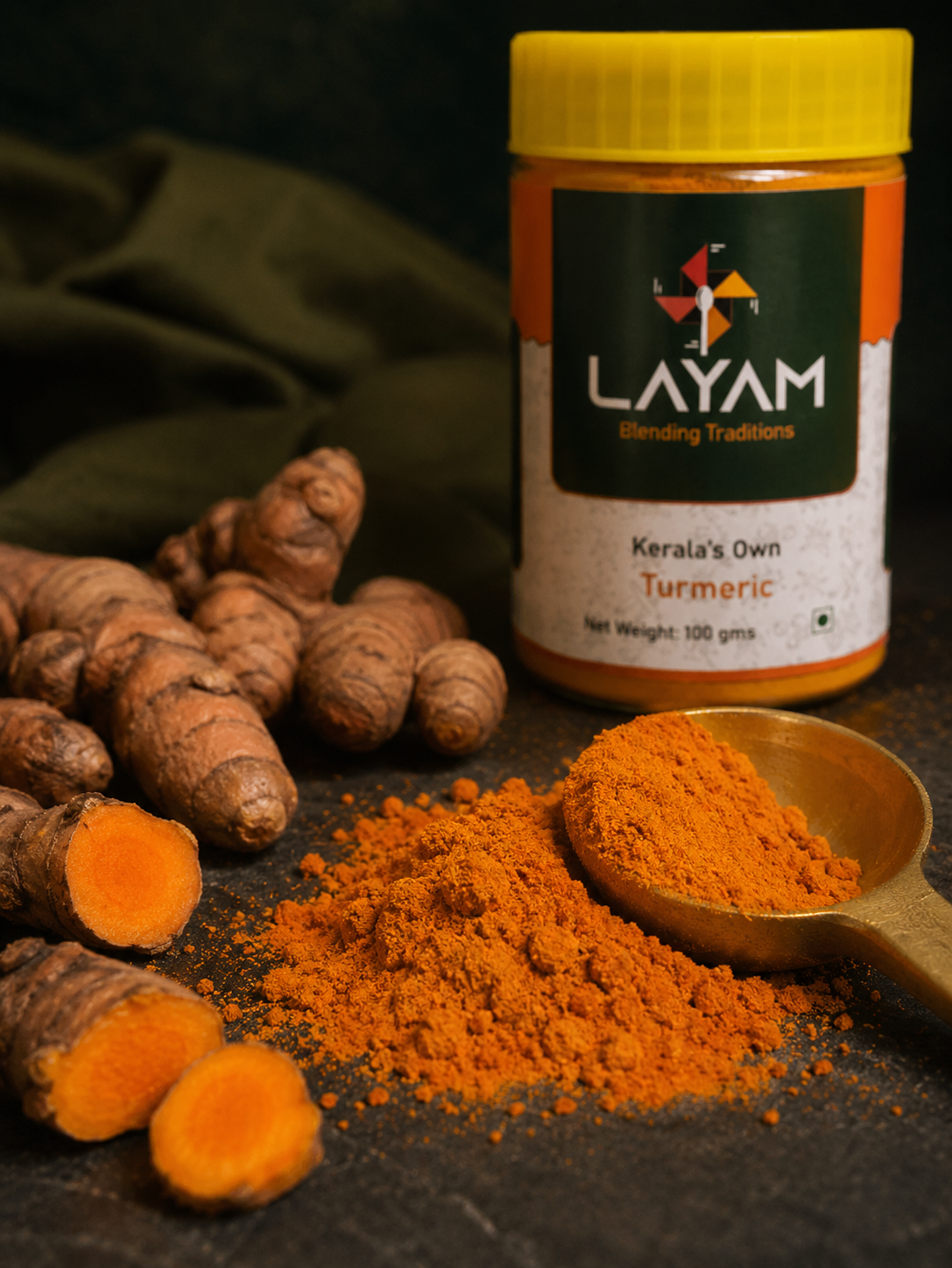 Close-up of deep golden LAYAM turmeric powder on a brass spoon beside cut fresh turmeric root